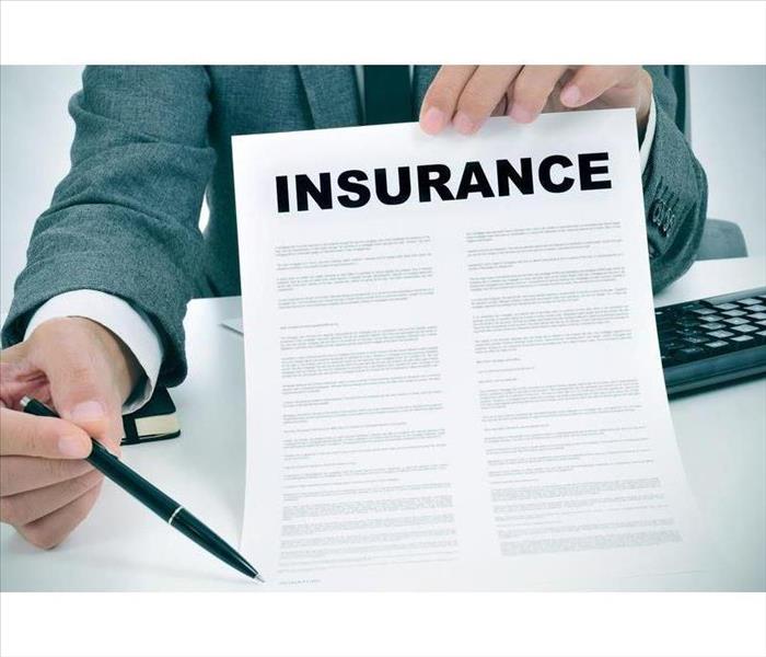 A man holding a sheet with his left hand, on top of the sheet it says "Insurance" with his right hand he has a pen