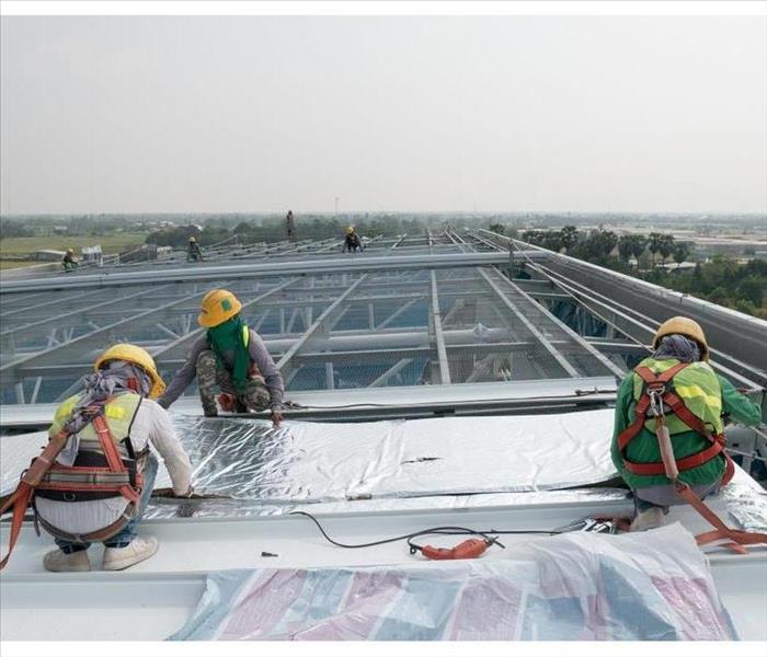 Construction worker wearing safety harness and safety line working on a metal industry roof 